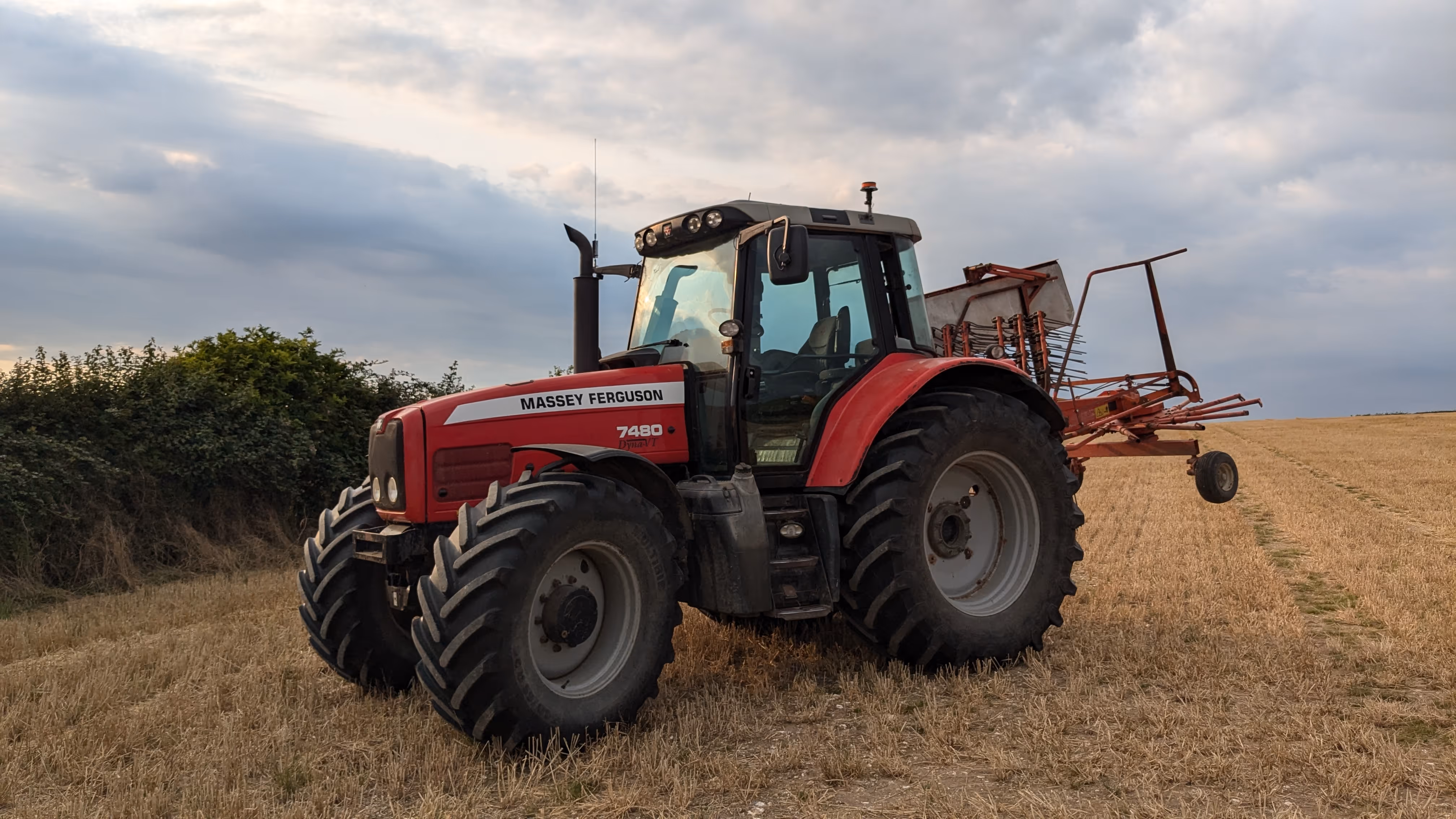 A massey Ferguson tractor in a field, fitted with a hay rake